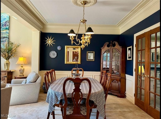carpeted dining area with a healthy amount of sunlight, a chandelier, wainscoting, ornamental molding, and french doors