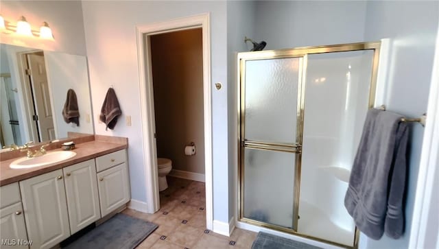 bathroom featuring vanity, tile patterned floors, toilet, a stall shower, and baseboards