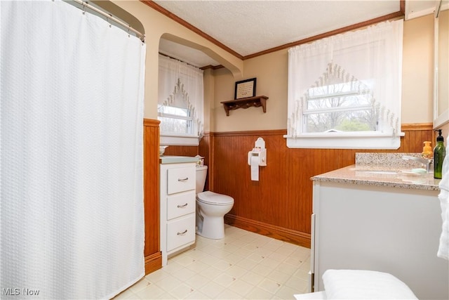 bathroom with ornamental molding, a wainscoted wall, toilet, and vanity
