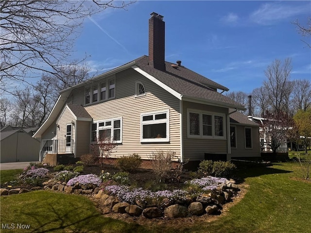 back of property featuring a chimney, a yard, and a shingled roof