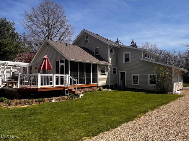 rear view of house with roof with shingles, a wooden deck, a sunroom, and a lawn