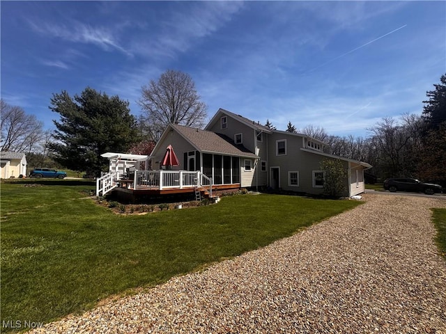 back of house with a sunroom, a wooden deck, a lawn, and gravel driveway