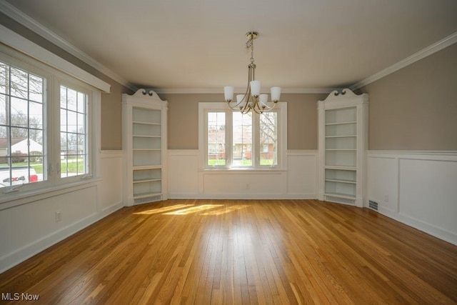 unfurnished dining area with an inviting chandelier, a wainscoted wall, crown molding, and wood-type flooring