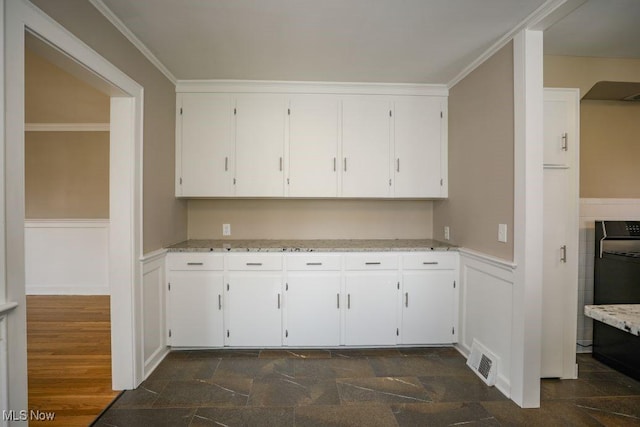clothes washing area featuring visible vents, ornamental molding, a wainscoted wall, and stone tile flooring