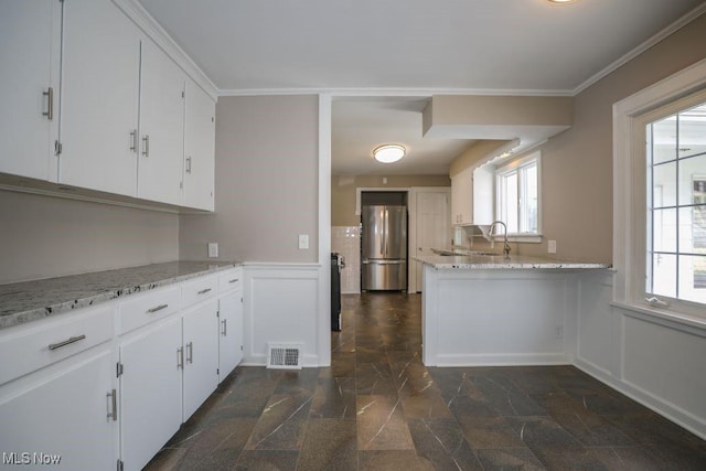 kitchen featuring a sink, white cabinets, visible vents, wainscoting, and freestanding refrigerator