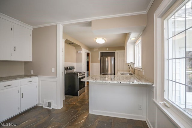 kitchen with wainscoting, appliances with stainless steel finishes, a sink, white cabinetry, and visible vents