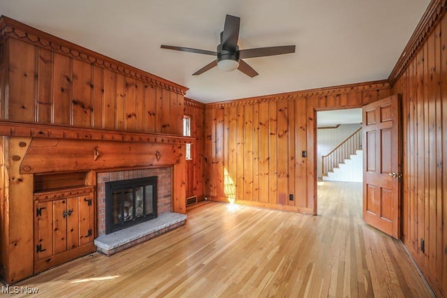 unfurnished living room with a fireplace, light wood-style floors, ceiling fan, wooden walls, and visible vents