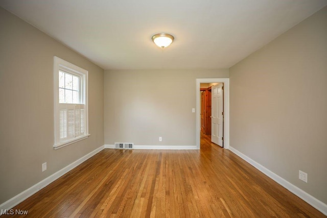 unfurnished room with baseboards, visible vents, and wood finished floors