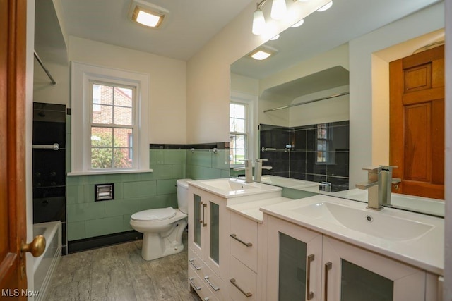 full bath featuring toilet, tile walls, wood finished floors, vanity, and wainscoting