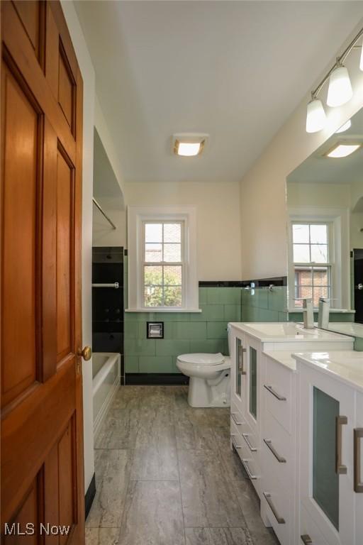 bathroom with tile walls, a healthy amount of sunlight, toilet, and vanity