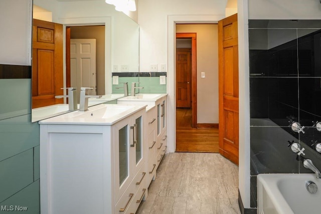 bathroom with two vanities, a tub to relax in, wood finished floors, and a sink