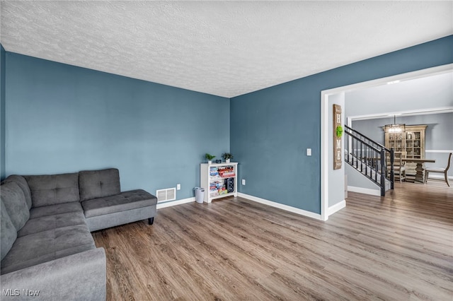 living area featuring stairway, a chandelier, visible vents, baseboards, and wood finished floors