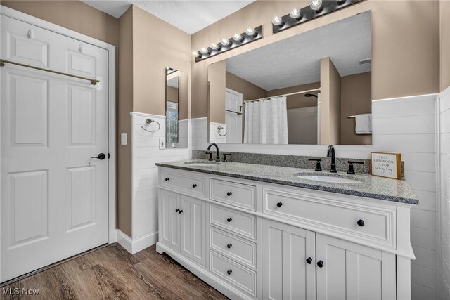 bathroom with a wainscoted wall, double vanity, a sink, and wood finished floors