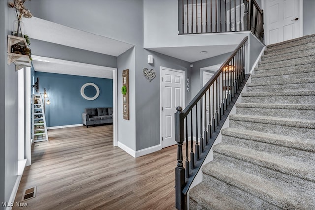 stairs with a towering ceiling, wood finished floors, visible vents, and baseboards