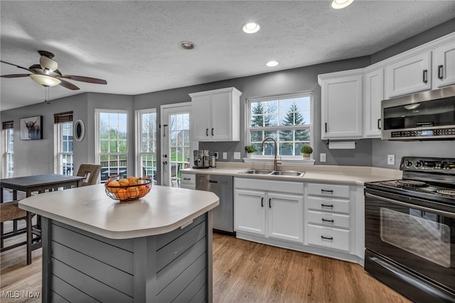 kitchen featuring a sink, appliances with stainless steel finishes, light countertops, a kitchen island, and light wood-type flooring