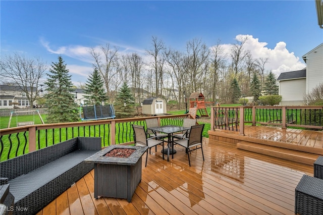 deck featuring a trampoline, an outdoor structure, a storage unit, outdoor dining space, and a playground