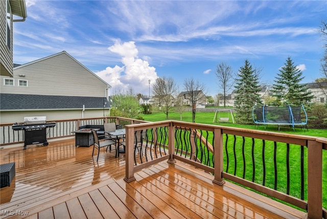 deck featuring a trampoline, outdoor dining space, area for grilling, and a yard