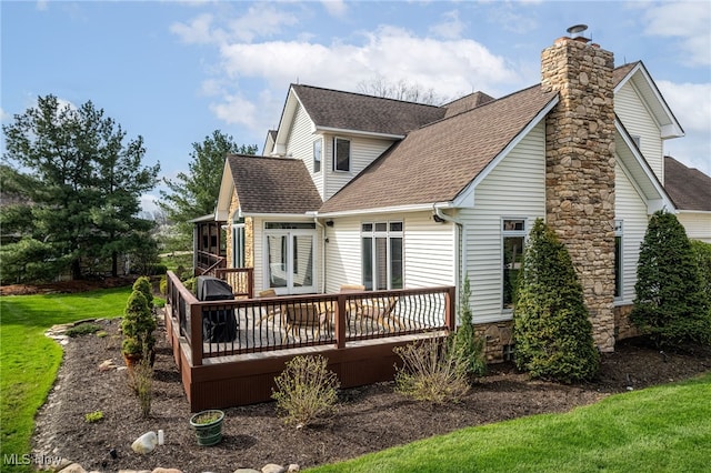 back of house with roof with shingles, a deck, a yard, and a chimney