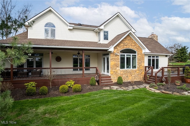 view of front of property featuring a chimney, ceiling fan, stone siding, roof with shingles, and a front yard