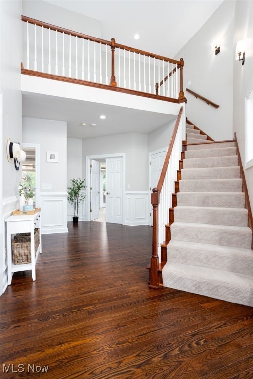 stairway with recessed lighting, a wainscoted wall, a decorative wall, a towering ceiling, and wood finished floors