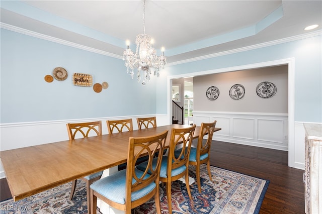 dining area featuring a chandelier, a raised ceiling, a wainscoted wall, ornamental molding, and wood finished floors