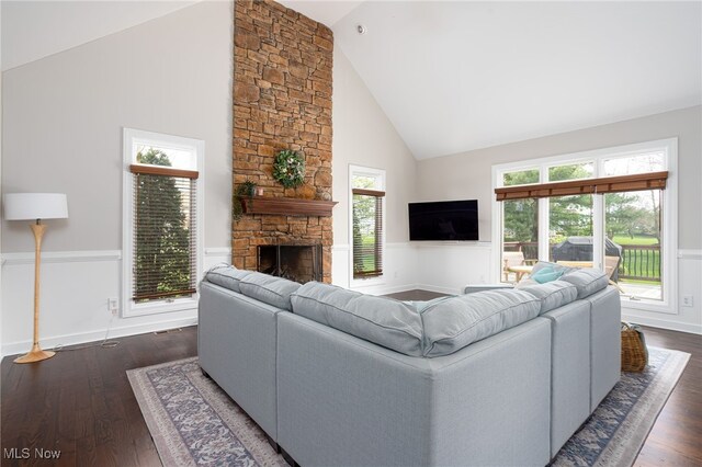 living room featuring a wainscoted wall, high vaulted ceiling, and a stone fireplace