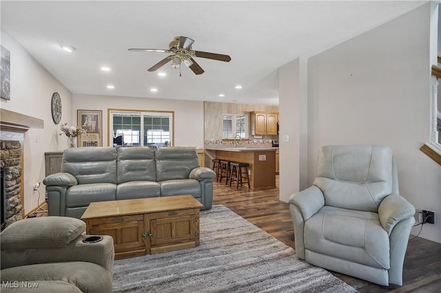 living room with recessed lighting, a ceiling fan, a stone fireplace, and dark wood-style flooring