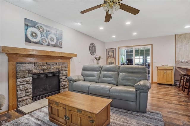 living area with wood finished floors, a ceiling fan, a stone fireplace, and recessed lighting