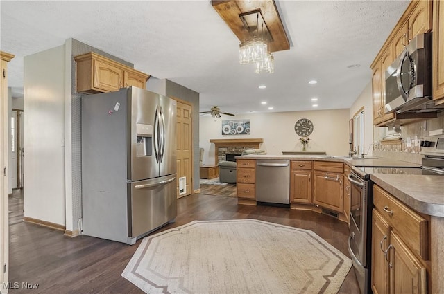 kitchen with dark wood-style flooring, a peninsula, appliances with stainless steel finishes, and a fireplace
