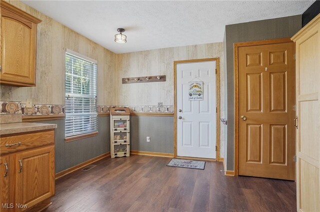 foyer entrance featuring baseboards, wallpapered walls, a textured ceiling, and dark wood-type flooring