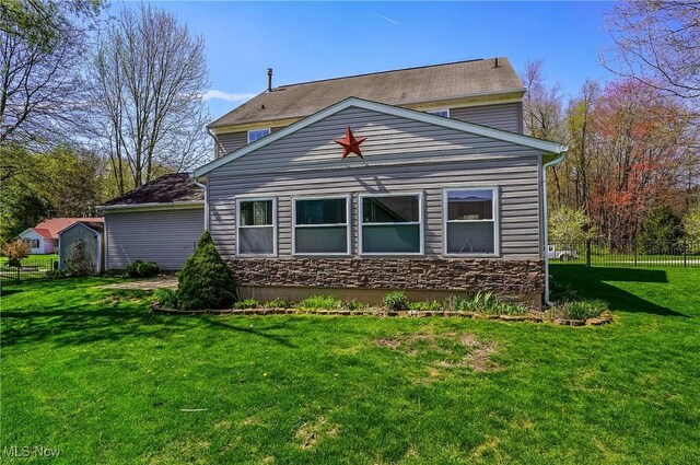 rear view of property featuring stone siding, fence, and a lawn