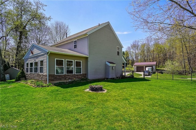 rear view of house with an outbuilding, an outdoor fire pit, a lawn, and fence