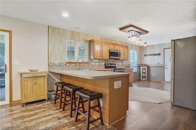 kitchen featuring a sink, stainless steel appliances, a kitchen bar, a peninsula, and wood finished floors