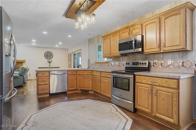 kitchen featuring dark wood finished floors, appliances with stainless steel finishes, light countertops, a sink, and a peninsula