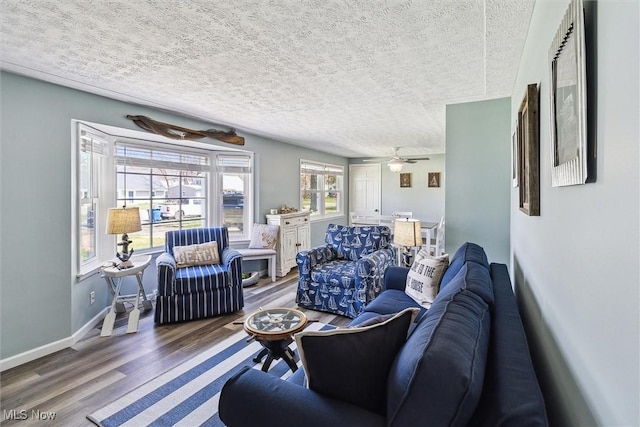 living room featuring baseboards, wood finished floors, ceiling fan, and a textured ceiling