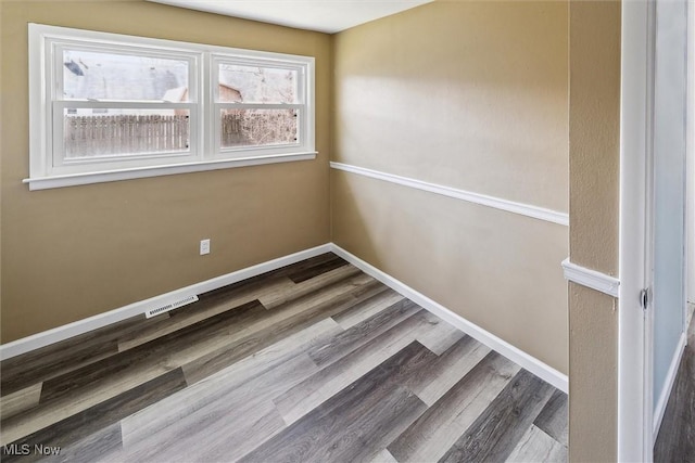 empty room with wood finished floors, visible vents, and baseboards