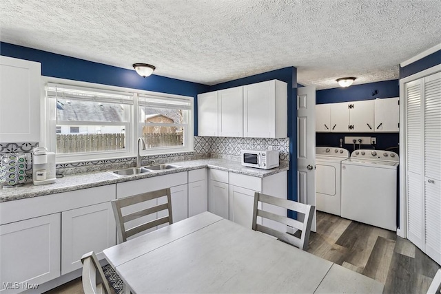 kitchen featuring dark wood-style floors, a sink, separate washer and dryer, white microwave, and white cabinetry