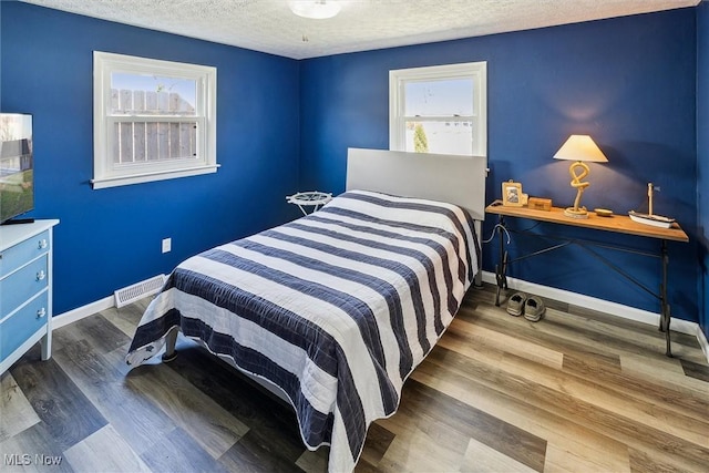 bedroom featuring a textured ceiling, visible vents, wood finished floors, and multiple windows