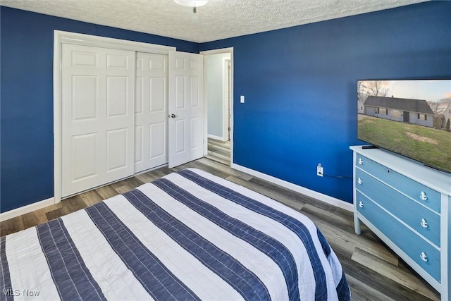 unfurnished bedroom featuring a textured ceiling, a closet, wood finished floors, and baseboards