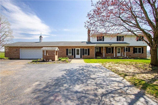traditional home featuring driveway, a porch, brick siding, and a garage
