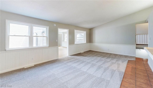 unfurnished living room featuring lofted ceiling, carpet, visible vents, and a wainscoted wall