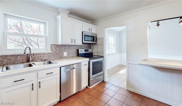 kitchen with light tile patterned floors, appliances with stainless steel finishes, a sink, white cabinetry, and crown molding