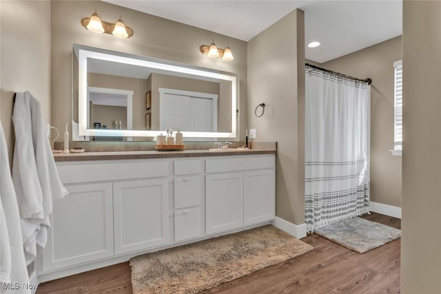 full bathroom featuring a sink, double vanity, a shower with shower curtain, baseboards, and wood finished floors