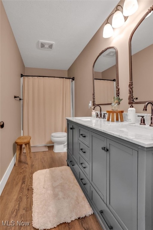 bathroom with wood finished floors, double vanity, toilet, a sink, and visible vents