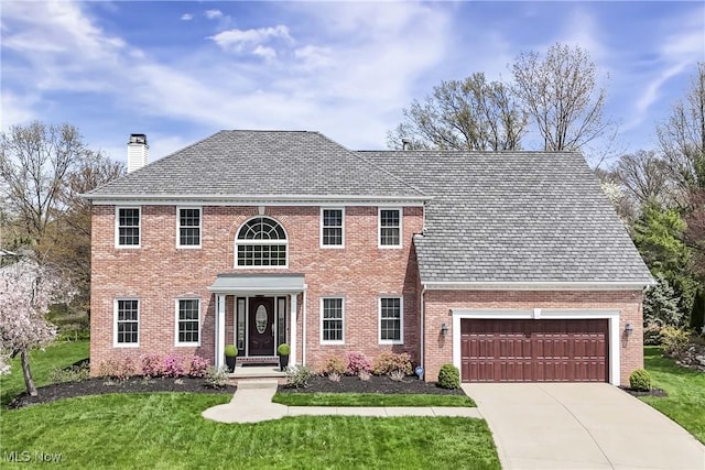 colonial-style house with a chimney, a high end roof, a garage, and a front lawn