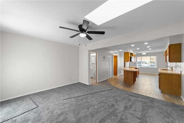 unfurnished living room featuring baseboards, a ceiling fan, carpet flooring, and a sink