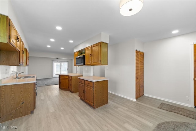 kitchen featuring stainless steel microwave, a sink, light countertops, light wood-type flooring, and brown cabinetry