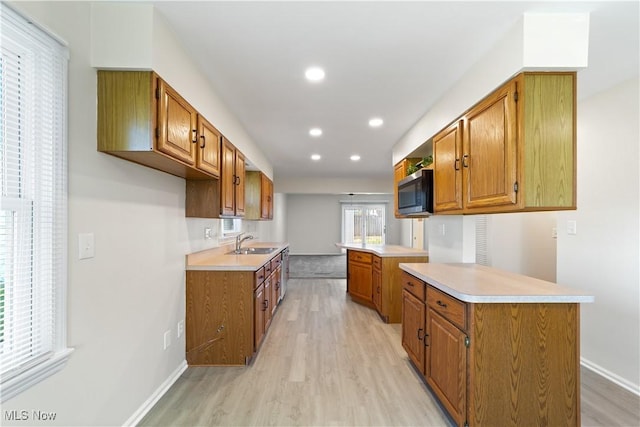 kitchen with stainless steel microwave, brown cabinetry, light wood-type flooring, a peninsula, and light countertops