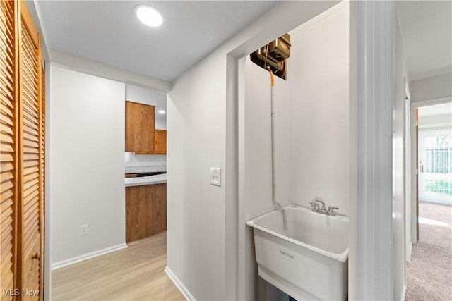 hall with a sink, light wood-style flooring, and baseboards