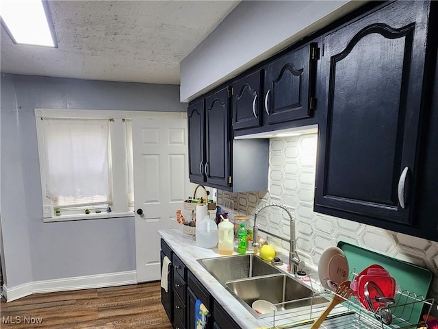 kitchen with baseboards, tasteful backsplash, light countertops, a sink, and dark wood-style floors